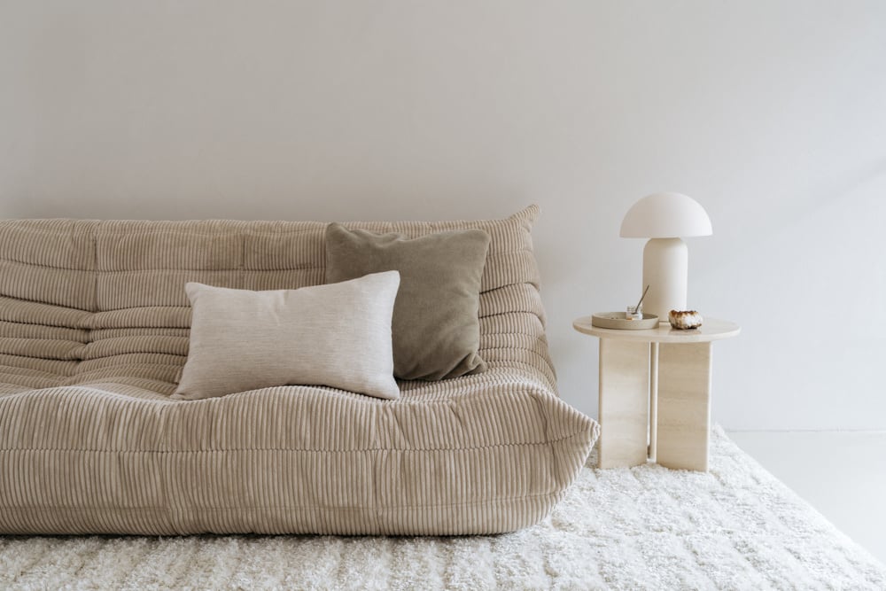 Travertin bijzettafel naast een beige bank gestyled met een room witte tafellamp in een modern interieur