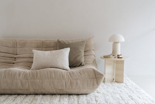 Travertin bijzettafel naast een beige bank gestyled met een room witte tafellamp in een modern interieur