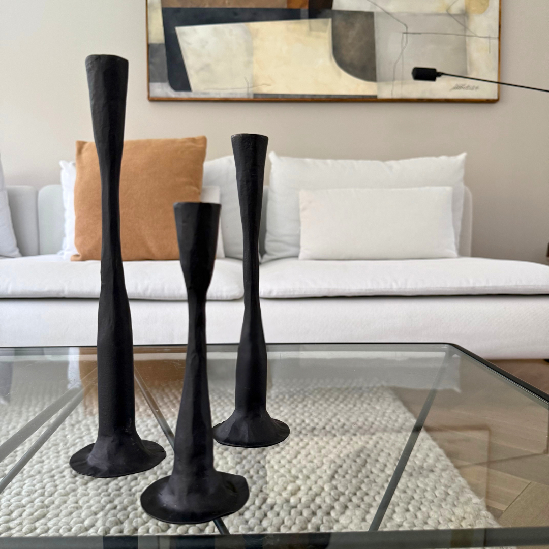 Drie zwarte gietijzeren kandelaars in verschillende hoogtes – speels en gebalanceerd op een glazen salontafel
