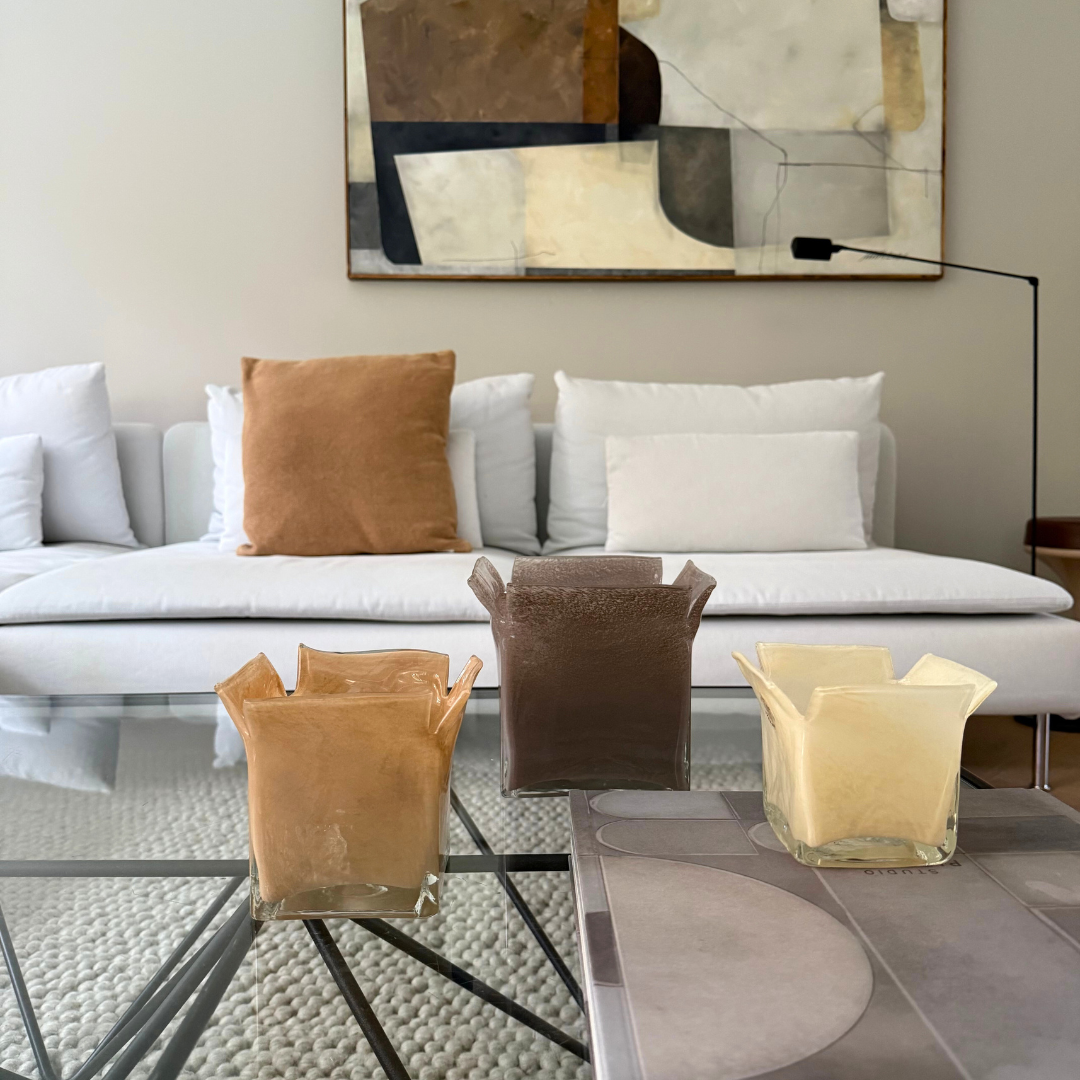 3 glazen Atlas kaarshouders in de kleuren taupe, zand en vanille gestyled op een glazensalontafel in een zithoek in natuurlijke tinten.