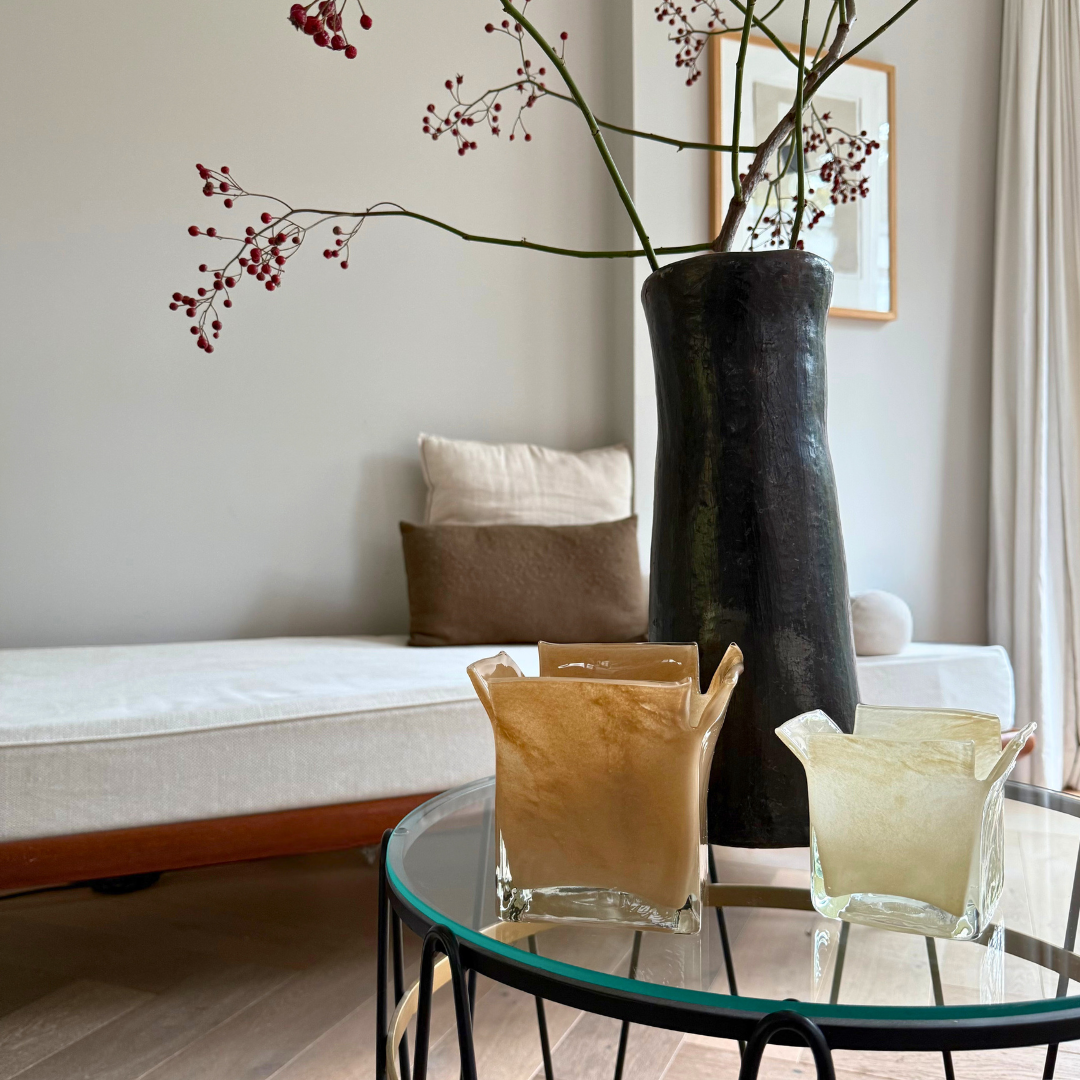 Atlas kaarshouders zand en vanille, gestyled met een zwarte handgemaakte vaas met een tak met rode besjes op een glazen bijzettafel