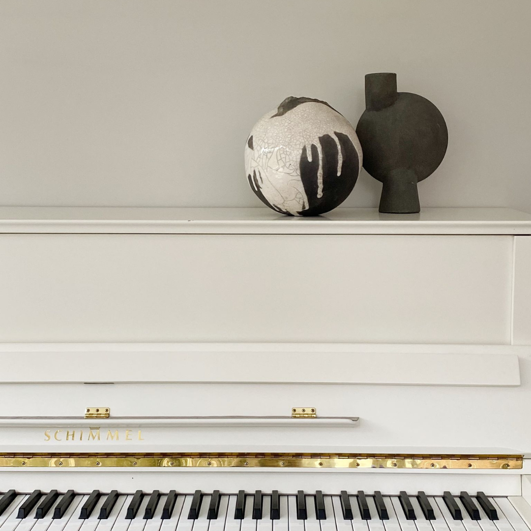 Bolvormige vaas van keramiek in creme en grijs tinten samen met een antraciet kleurige vaas op een witte piano