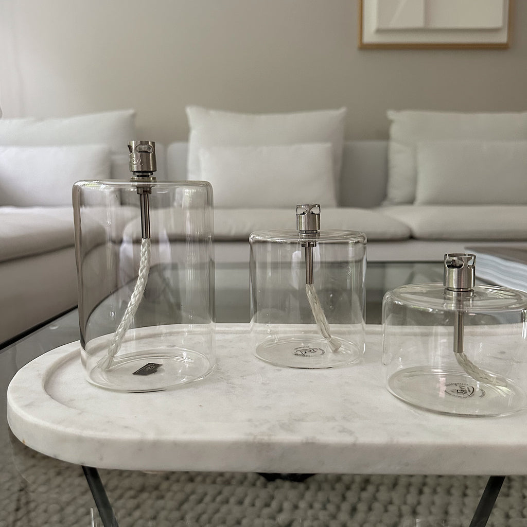 Drie elegante cilinder vormige transparant glazen olielampen van Peri Living op een wit marmer tray van Bloomingville in een minimalistisch interieur met neutrale tinten