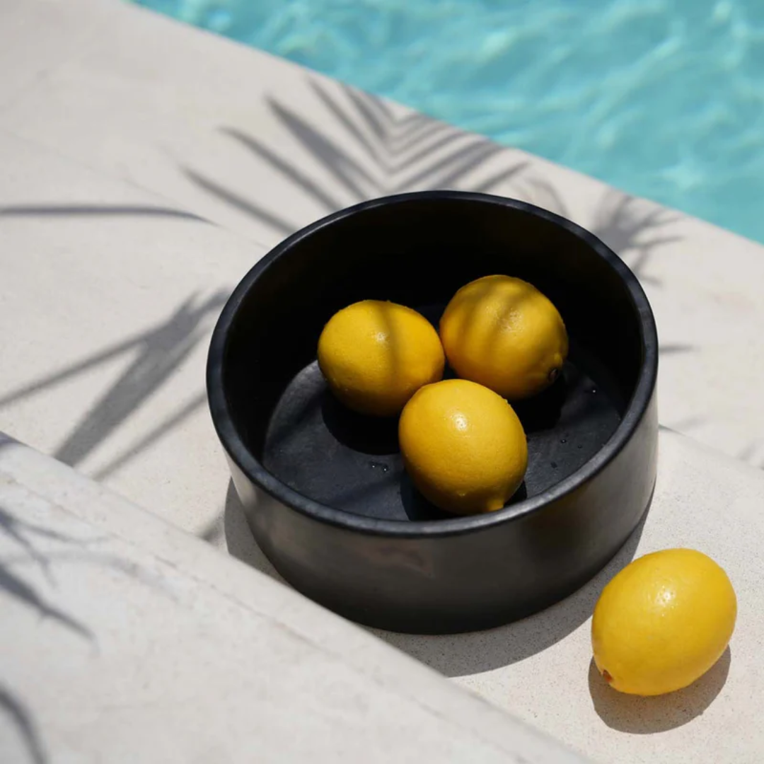 Zwarte kom uit de Burned collectie van Bazar Bizar gevuld met citroenen in een zomerse setting