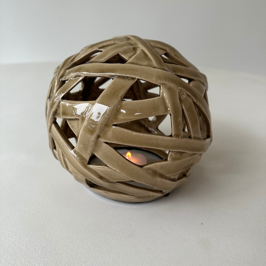 Vintage keramisch sculptuur met een brandend theelichtje eronder waardoor het kaarslicht zich verspreidt door de open structuur