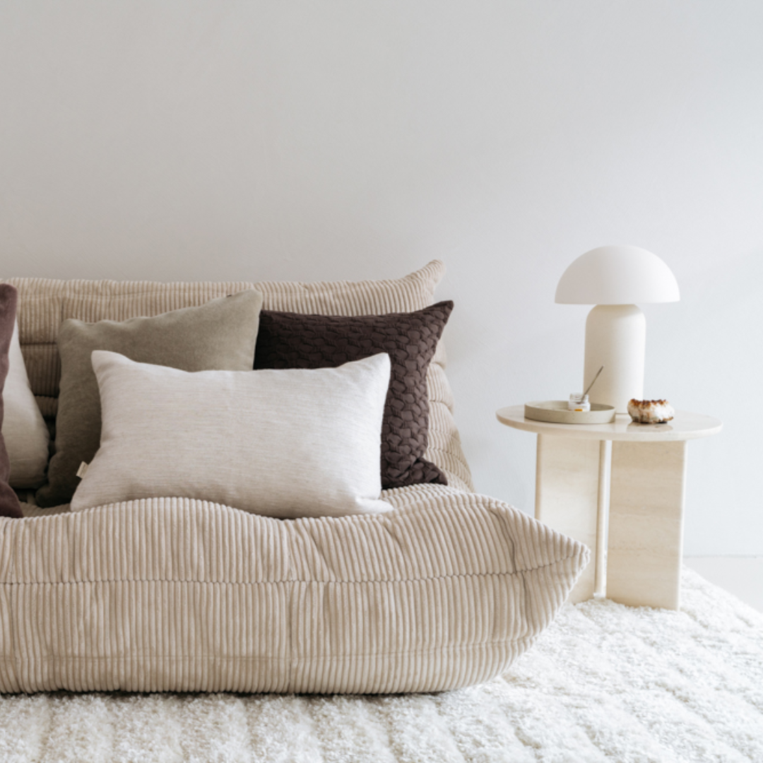 Ella kussenhoes gecombineerd met andere neutrale kussens op een beige bank in een modern minimalistisch interieur.