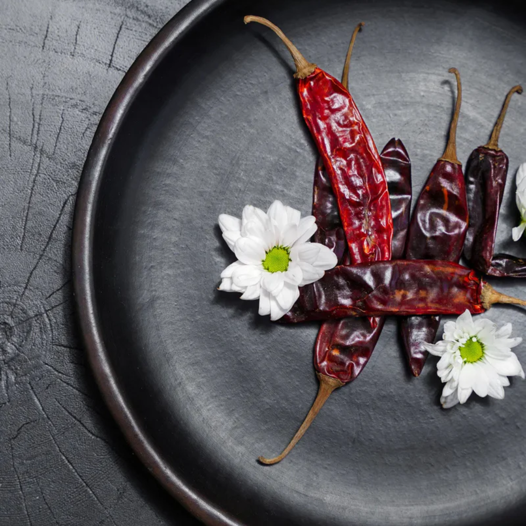 Close Up van het Burned Classic Bord van Bazar Bizar, gestyled met rode pepers en witte bloemetjes.