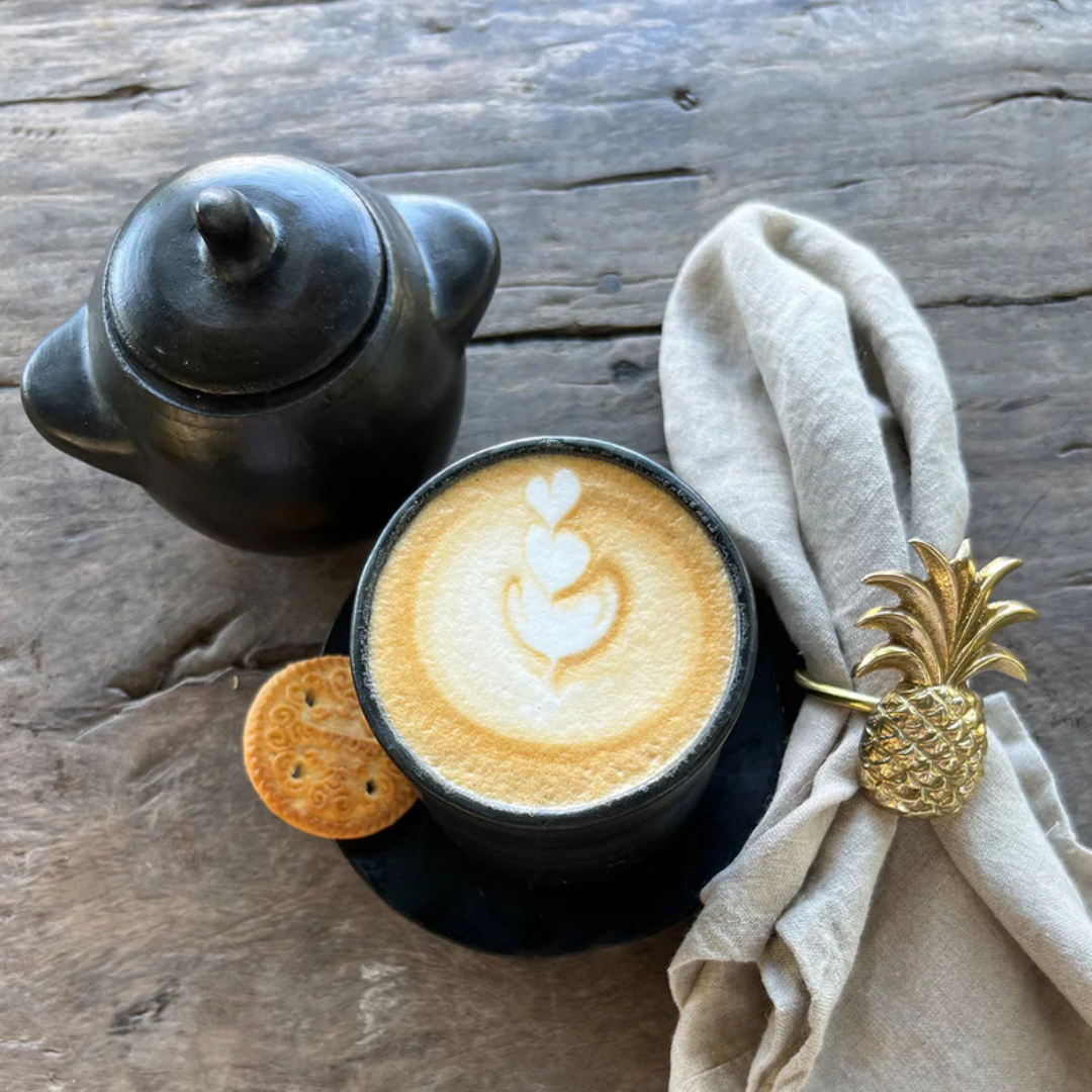 Burned Potje S gebruikt suikerpotje naast een cappuccino op houten tafel.