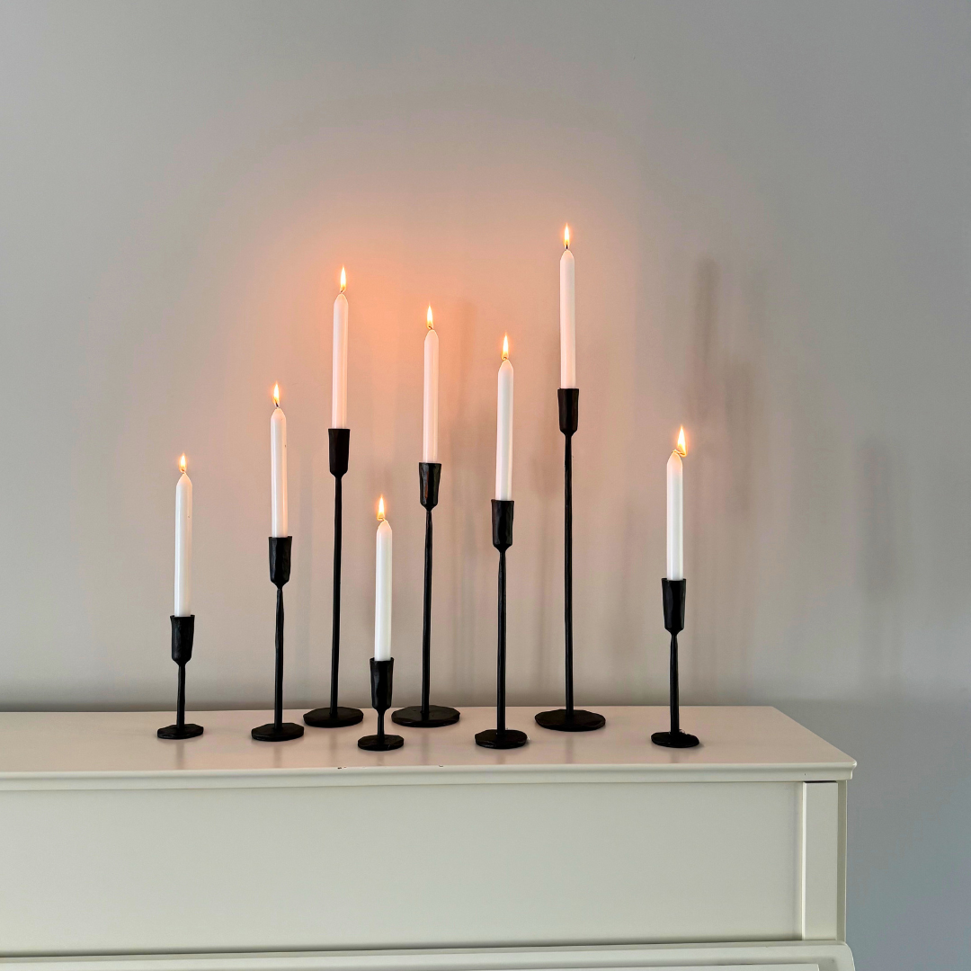 Minimalistische zwart metalen kandelaren van verschillende afmetingen met witte brandende kaarsen op een witte kast