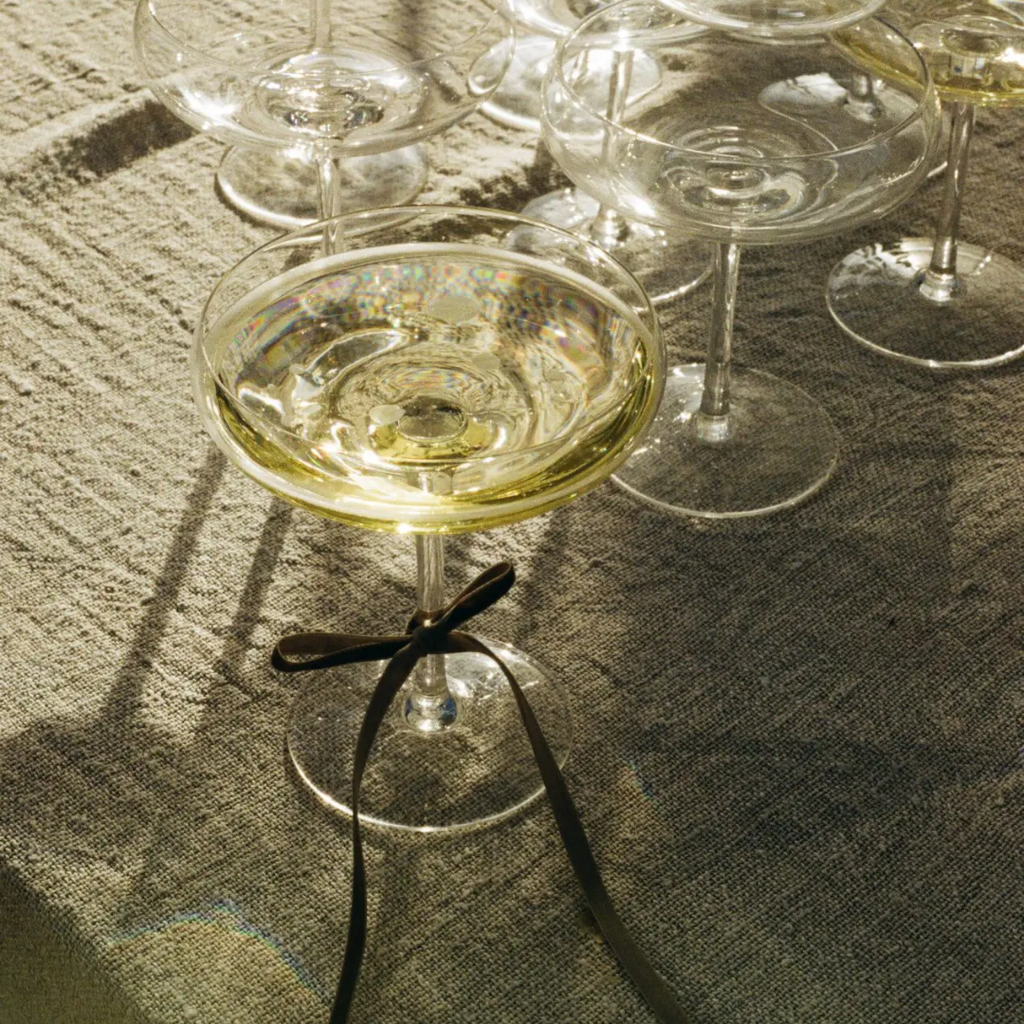 Mimosa glas met een strikje om de voet, gevuld met champagne samen met andere mimosa glazen op een linnen tafelkleed – perfect voor een feestelijk moment