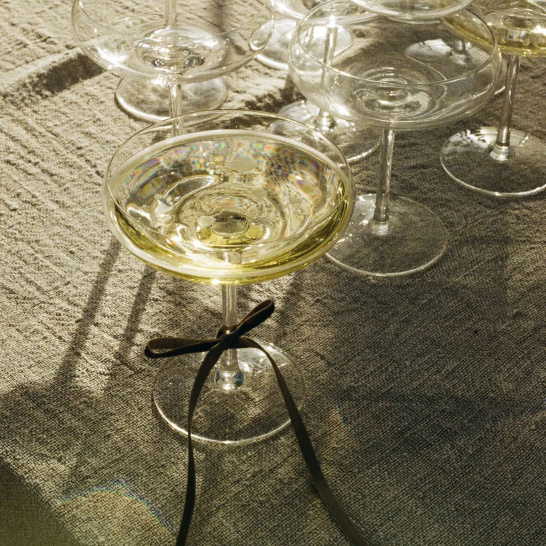 Mimosa glas met een strikje om de voet, gevuld met champagne samen met andere mimosa glazen op een linnen tafelkleed – perfect voor een feestelijk moment