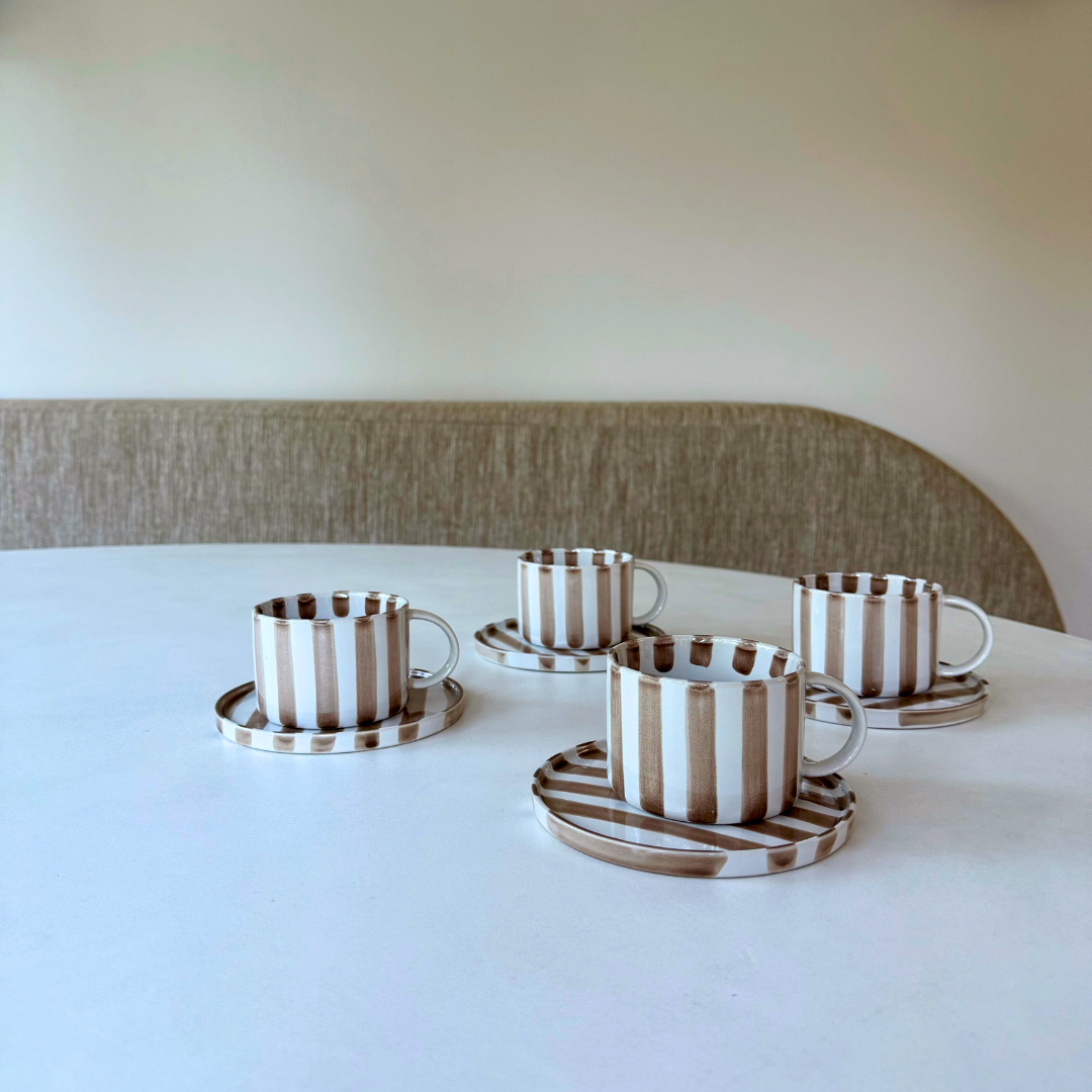 4 Monica kop en schotels met handgeschilderd gestreept beige-wit patroon op een witte tafel.