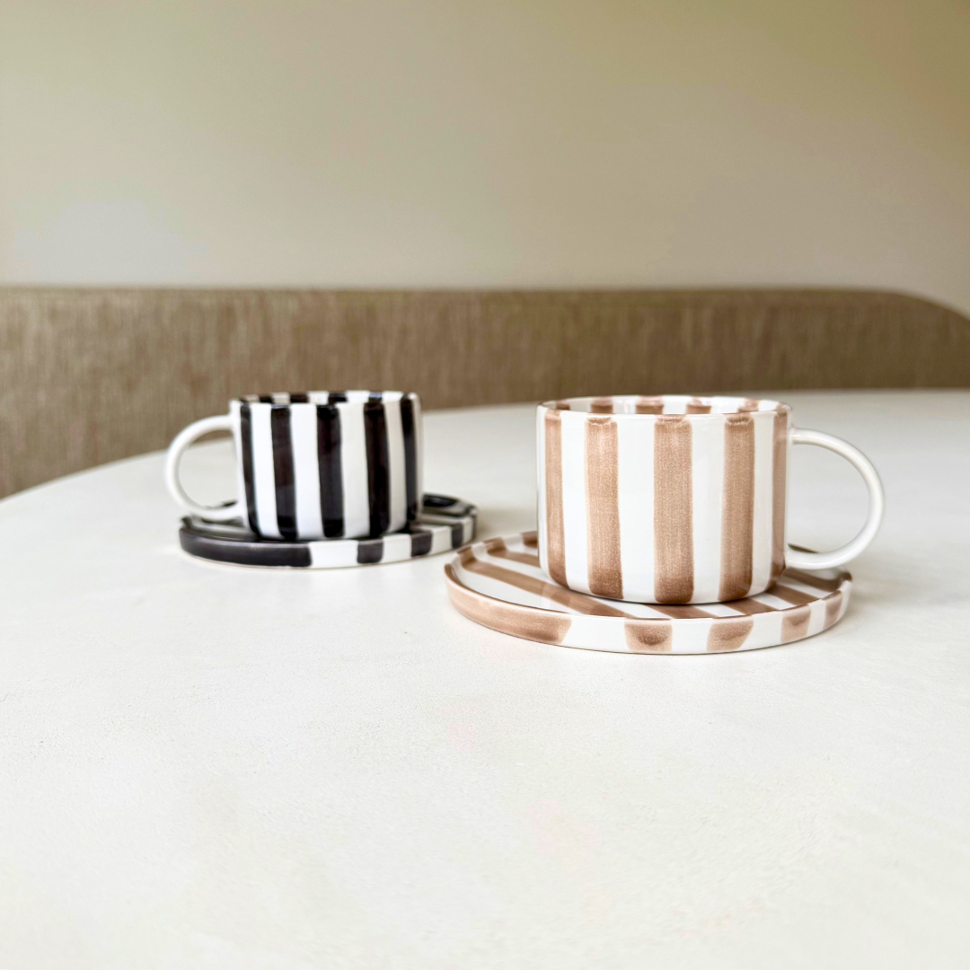 2 gestreepte kop en schotels op een witte eettafel, een in zwart-wit en de ander in beige-wit. Model Monica van Olsson & Jensen