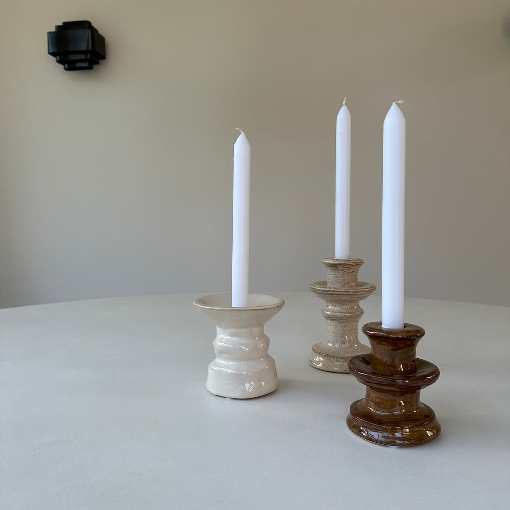 Stijlvolle beige keramieken kandelaar met witte kaars gecombineerd met een donkerbruine en een ecru kleurige kandelaar in een minimalistisch interieur