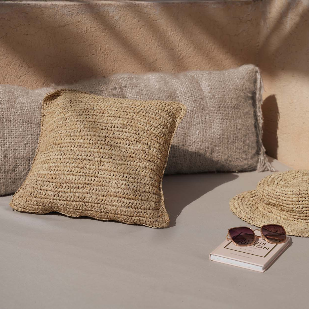 Raffia Flores Kussenhoes in combinatie met een ander kussen en een raffia zonnehoedje en zonnebril op een loungebank