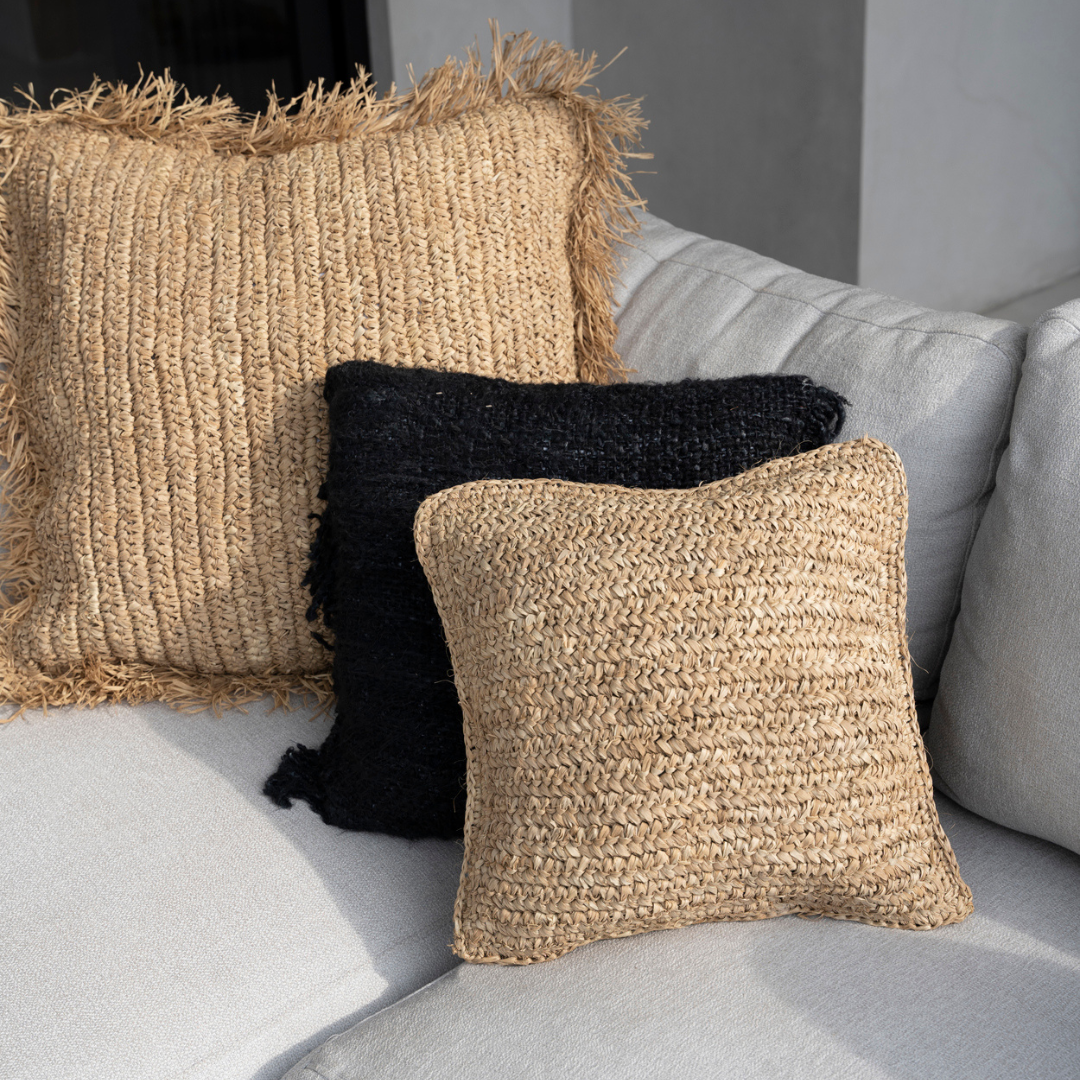 De Raffia Flores Kussenhoes gecombineerd met 2 andere kussens van natuurlijk materiaal van Bazar Bizar op een lichte bank