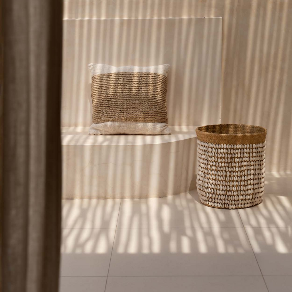 Raffia Stamp kussenhoes als decoratief accent op een neutrale buiten bankje naast een mand van natuurlijke materialen