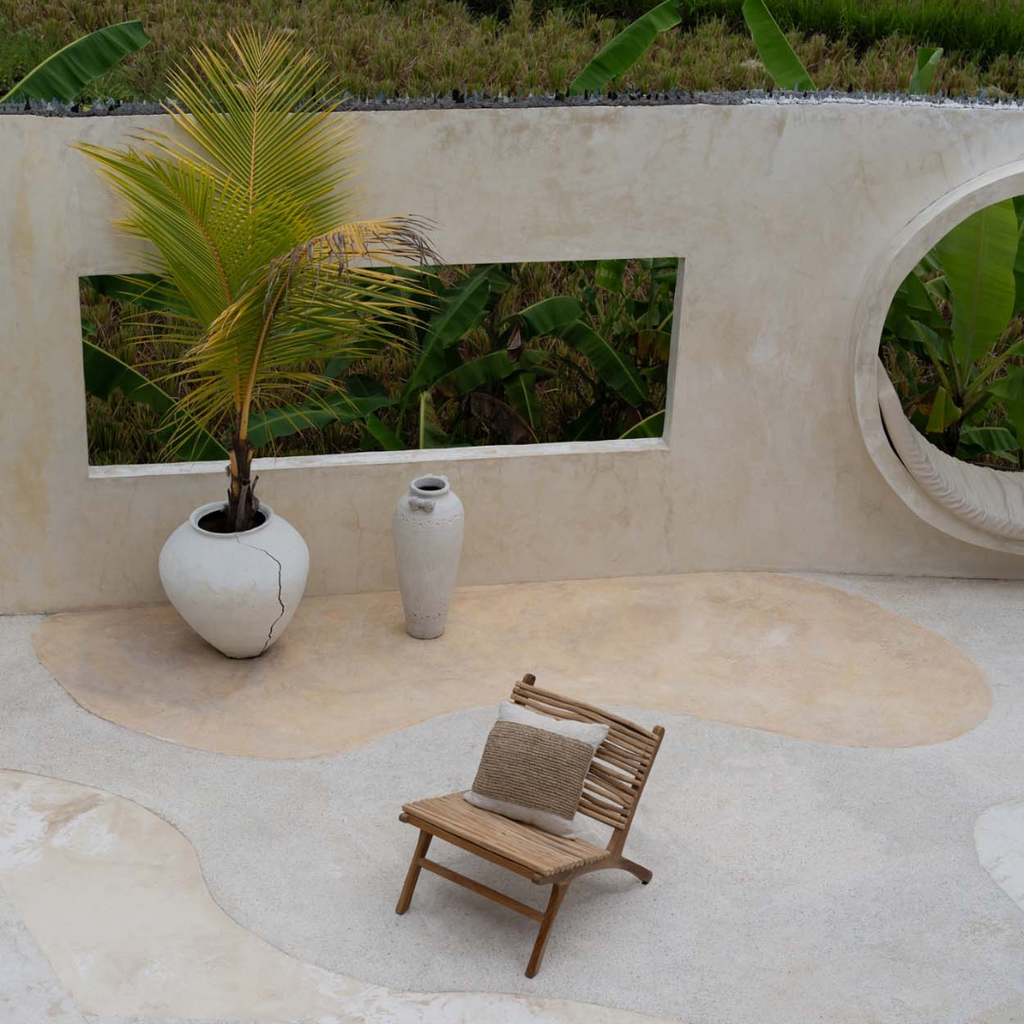 De Raffia Stamp Kussenhoes op een tuinstoel op een terras met een palmboom