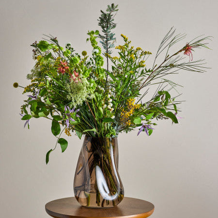 Transparant bruine organisch gevormde glazen vaas van Bloomingville, gevuld met een veldboeket