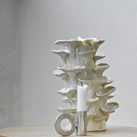 zilver kleurige apart gevormde kaarsenhouder met een rond oor met op de achtergrond een decoratieve witte vaas