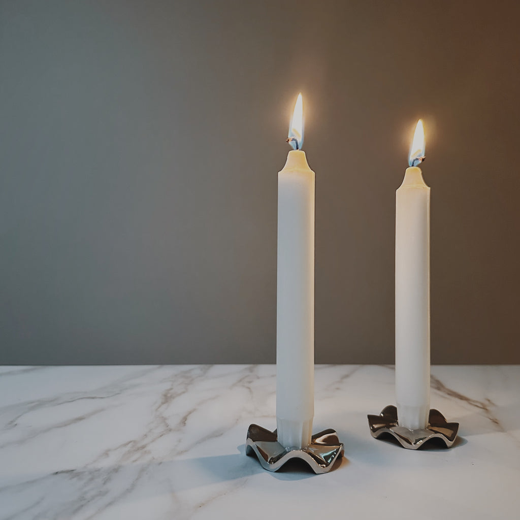 Set van twee zilver messing Signe kandelaars gestyled met brandende kaarsen op een marmer keukenblad