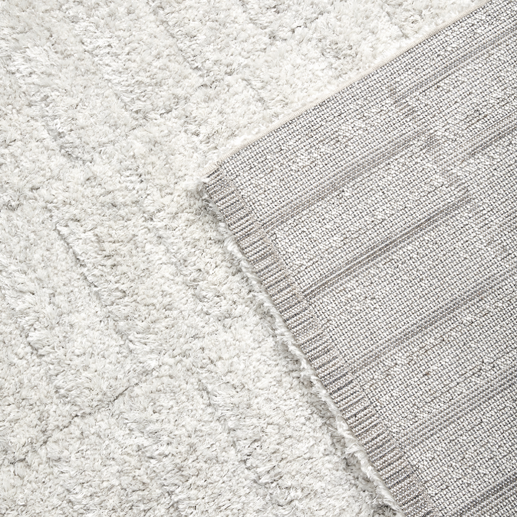 Detailopname van de festonsteek afwerking aan de lange zijde van het Stella vloerkleed en met zicht op de jute backing en omgeplooide korte zijde