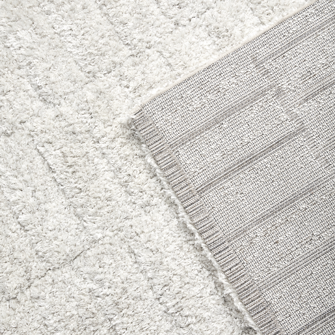 Detailopname van de festonsteek afwerking aan de lange zijde van het Stella vloerkleed en met zicht op de jute backing en omgeplooide korte zijde
