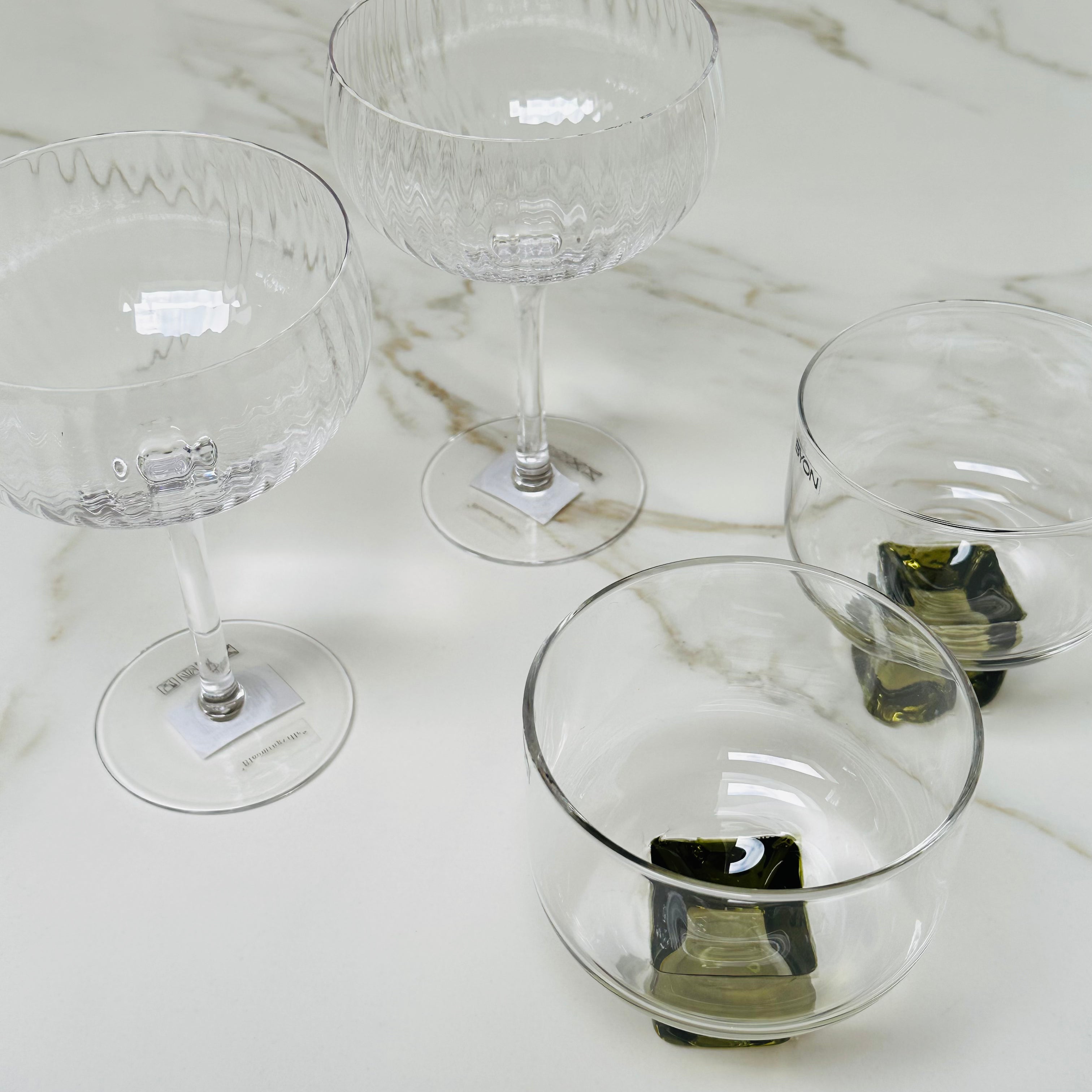 Set van 2 Byon Victoria glazen met groene voet en 2 Bloomingville Astrid champagne glazen op een marmeren oppervlak