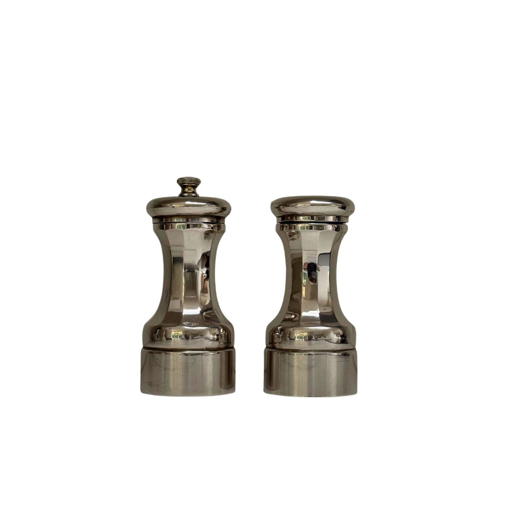 Vintage peper- en zoutstel van zilverkleurig metaal met getailleerde vormen, vrijstaand gefotografeerd.