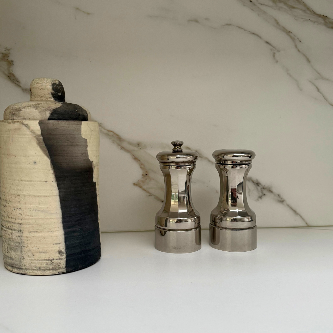 Vintage peper- en zoutstel van zilverkleurig metaal naast een zwart-witte keramieken pot.