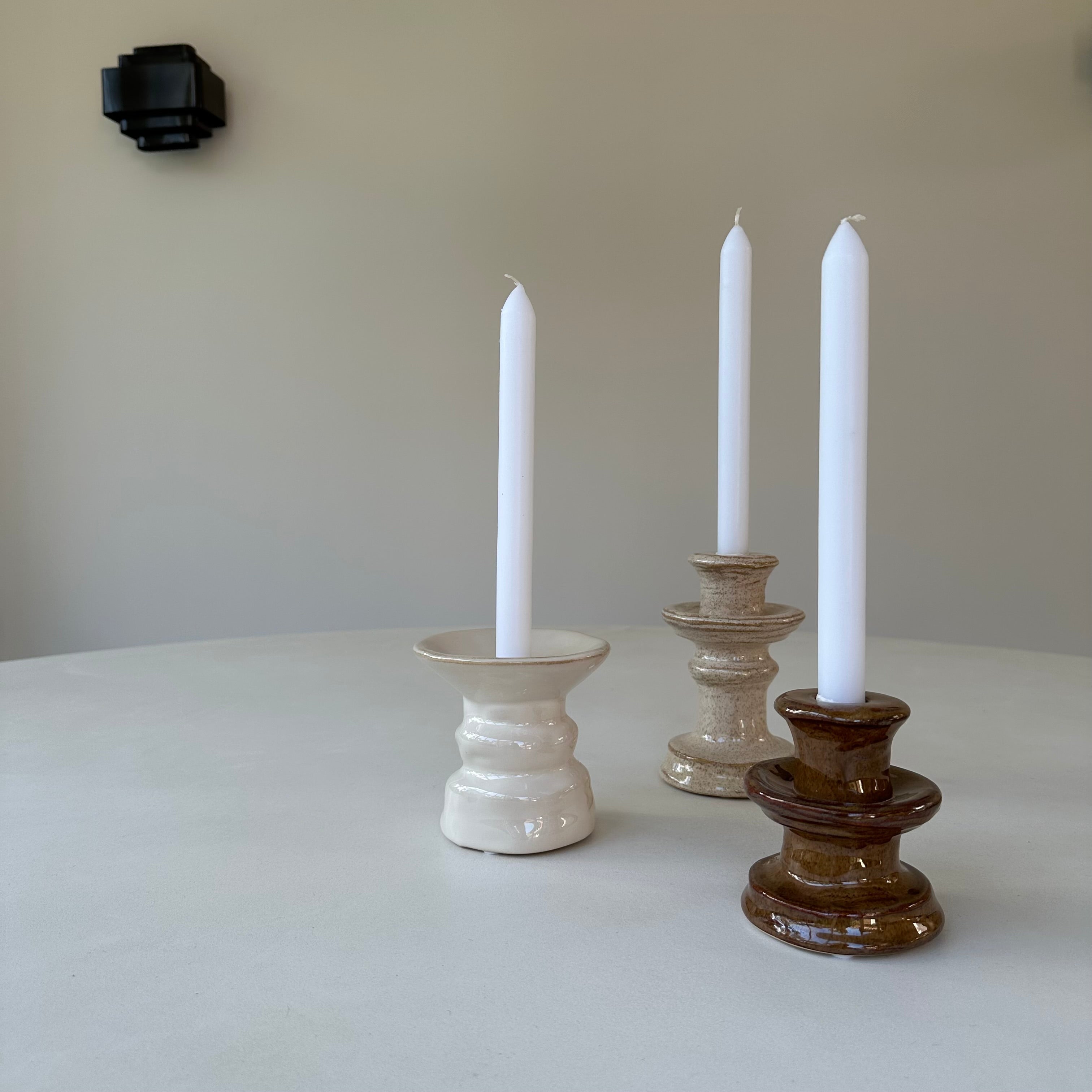 Stijlvolle minimalistische setting met de Zand Kandelaar en andere keramieken kandelaars met witte kaarsen